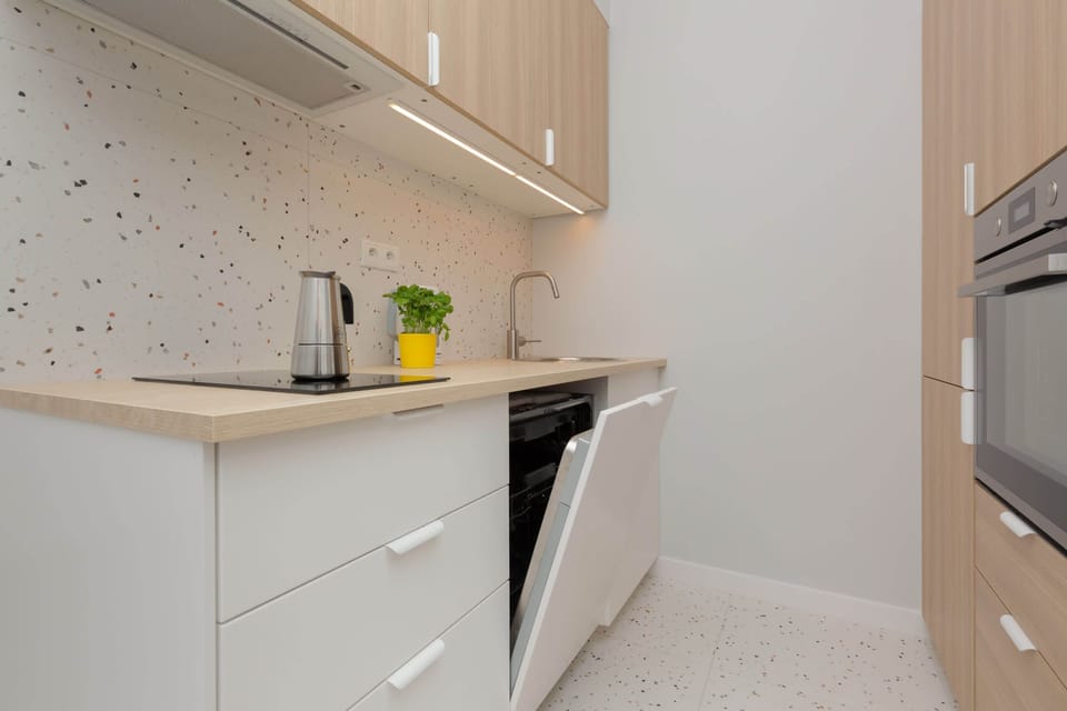 Kitchenette with bright furniture and quality appliances. There are fruit and an electric kettle on the wooden counter.
