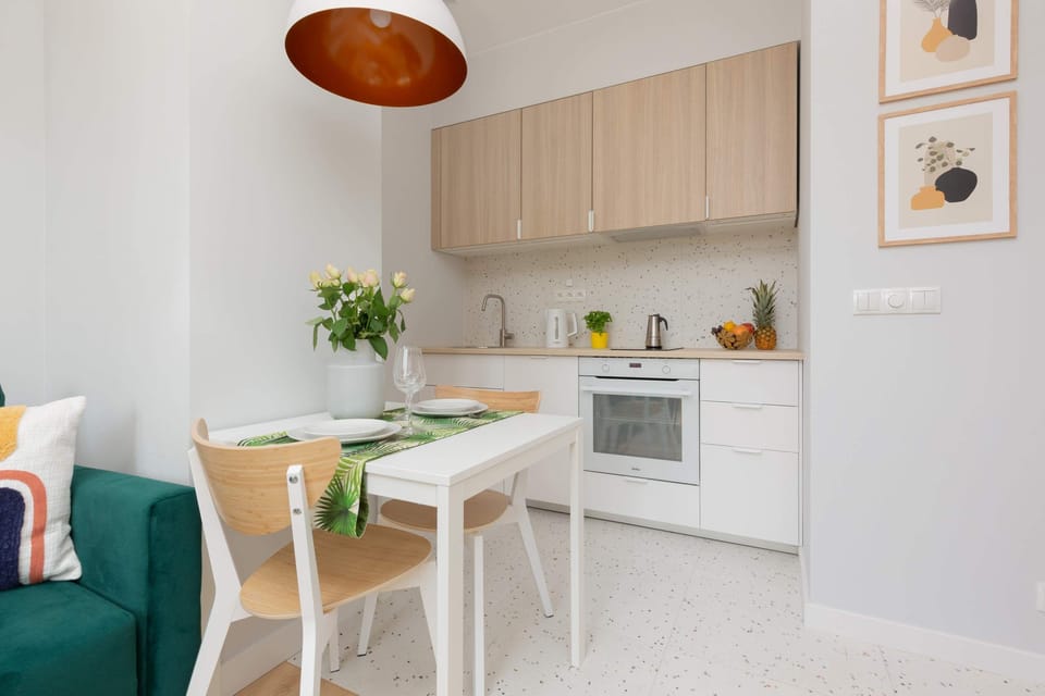 The functional kitchenette space has high-quality appliances. There is a white dining table next to it.