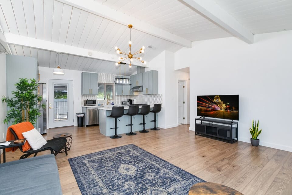 Stylish open-concept living area featuring a modern kitchen with a breakfast bar, a comfortable sectional sofa, and a contemporary chandelier, perfect for relaxing and entertaining.