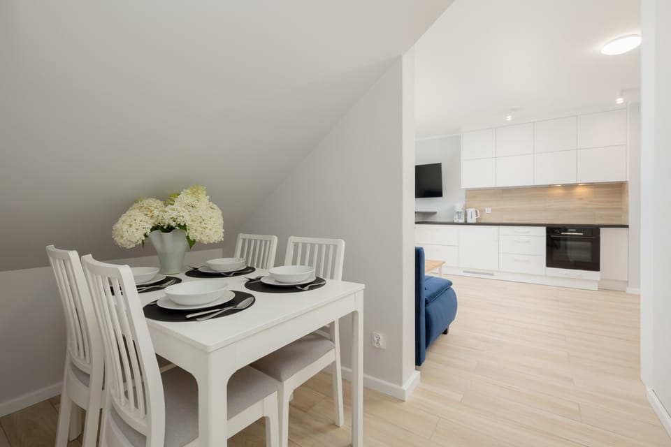 Dining area with white table with four chairs. The table has a vase of flowers and tableware for four people.