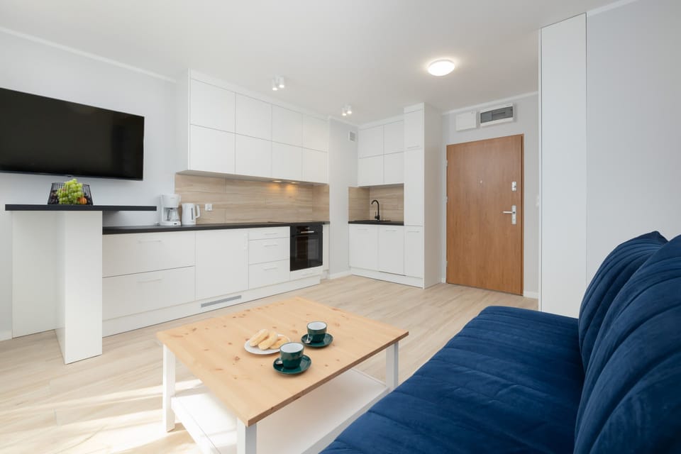 A view of the living and kitchen areas with a light wood floor, white furniture, and ample lighting.