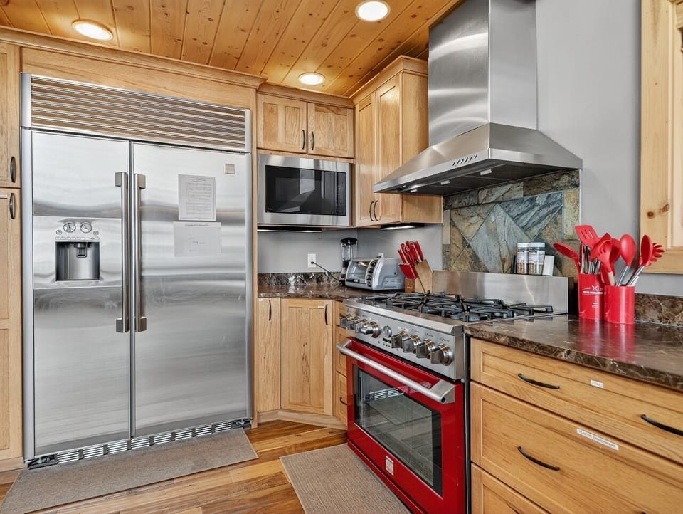 Your fully equipped gourmet kitchen features warm wood cabinetry, stainless steel appliances, and striking red accents that inspire culinary adventures.
