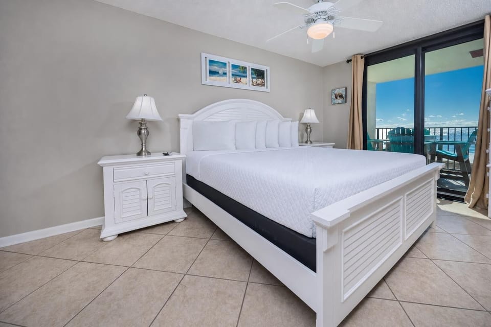 Charming master bedroom features a king bed, bedside lamps, and access to a balcony with views of the beach