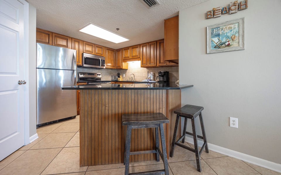 Modern kitchen with wooden cabinetry, sleek countertops, stainless appliances, coffee station, and a breakfast bar