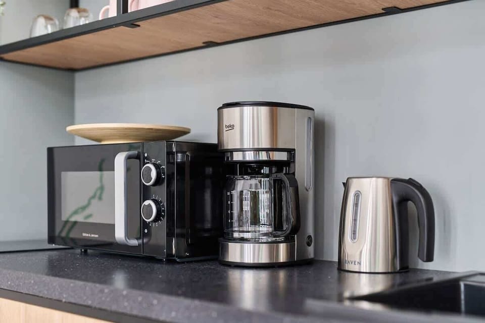 A modern kitchen with a coffee machine, kettle, and minimalist shelving.