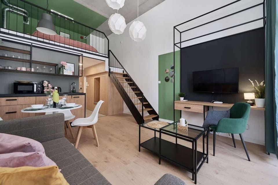 A spacious area featuring a living room with a sofa and a small kitchen with light wooden cabinetry and green accents.