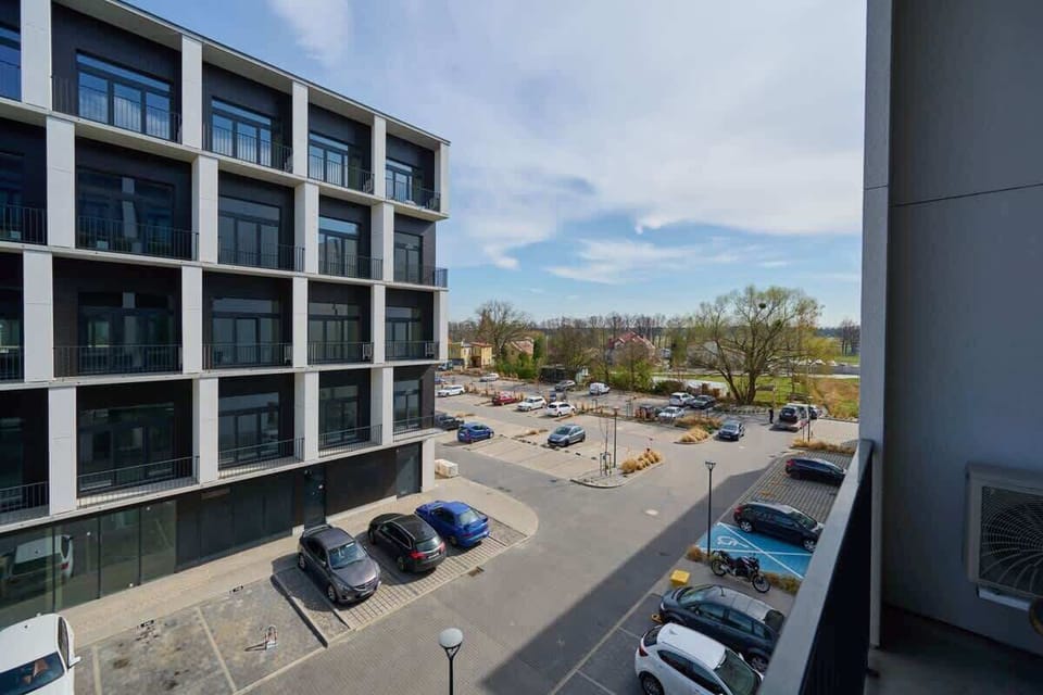 A perspective showing the exterior of modern apartments with parking spaces and surrounding urban landscape.