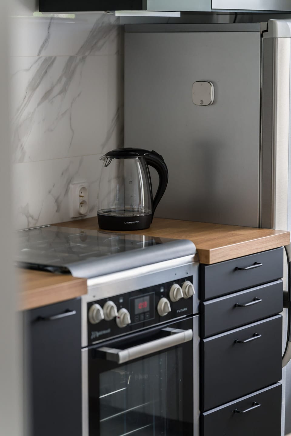 A compact kitchen with an oven, kettle, and a gray backsplash adding a sleek look.
