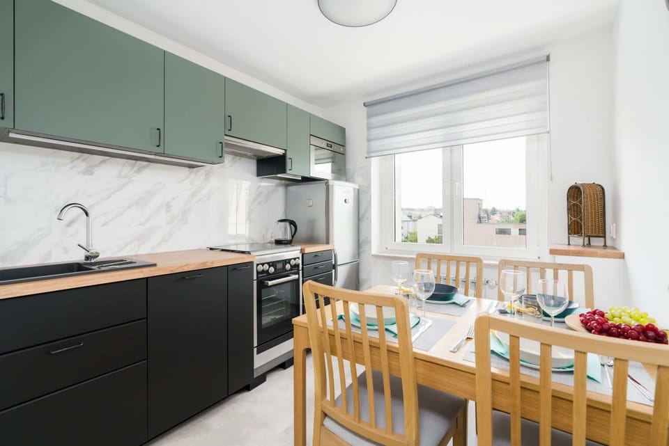 A modern kitchen with green cabinets, white countertops, and a dining table for four.