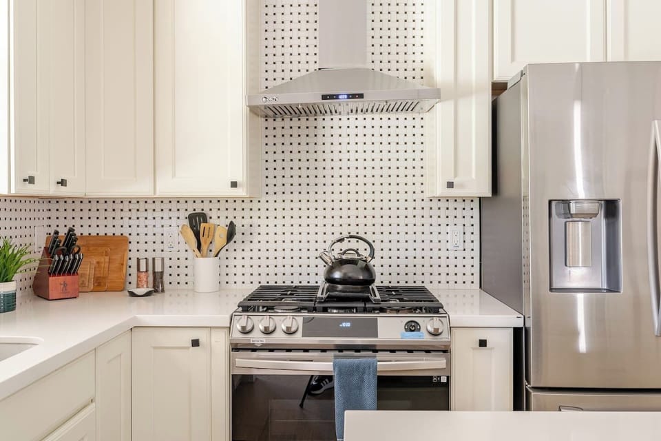 Prepare meals in style with a premium stainless steel gas range, complemented by chic black and white tile backsplash and modern cabinetry.