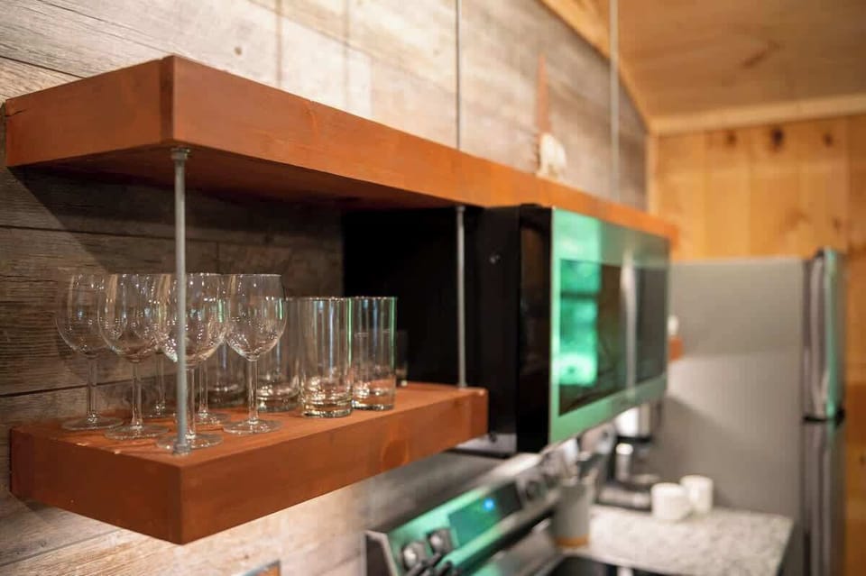 Open wooden shelving stocked with wine and water glasses adds both style and convenience to this modern rustic kitchen.