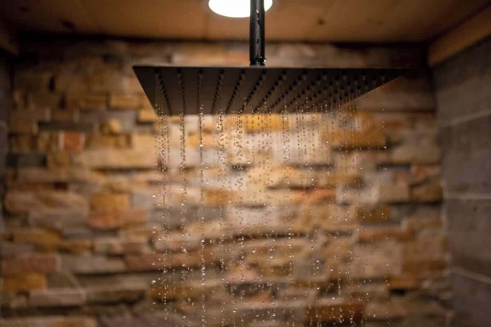 Close-up of the rainfall showerhead in action, offering a spa-like experience against a backdrop of natural stone tile.