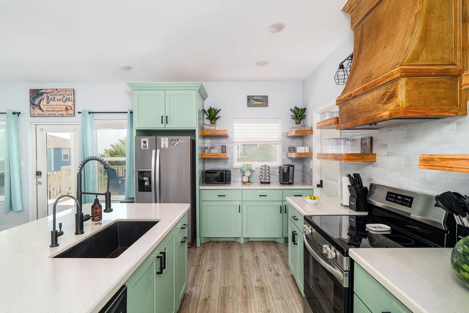 Kitchen detail — coastal green cabinetry, stocked utensils, full-size appliances. Cook like you're home.