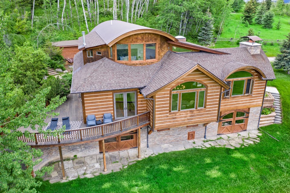 Rustic chalet with wraparound deck, lush greenery, and serene mountain charm.