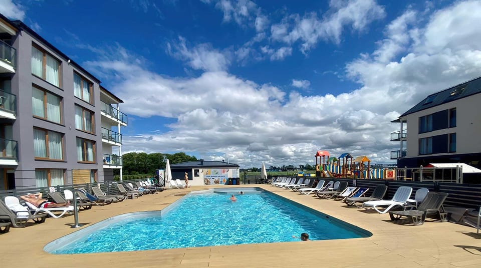 An outdoor pool surrounded by sun loungers and modern apartment buildings, perfect for relaxation.
