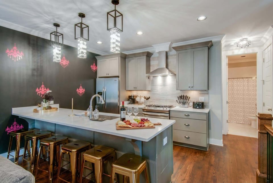 The kitchen island becomes the gathering spot: five bar stools line up under pendant lights while the cook stays in the mix at the stove