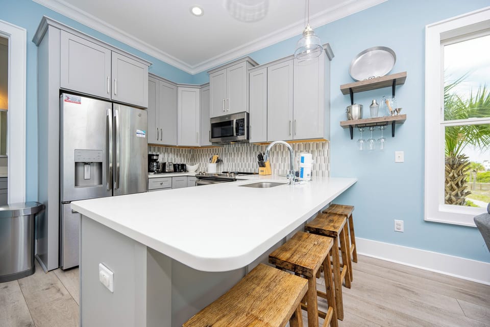 This kitchen features sleek stainless appliances, a bright white countertop, and a cozy seating area with a lagoon view