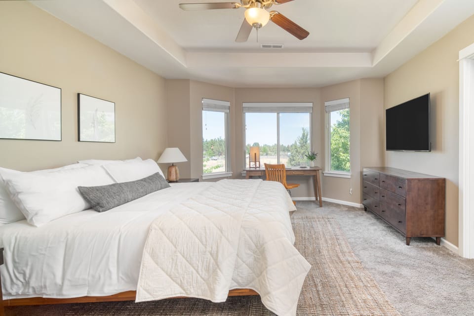 Primary bedroom features a king bed, ensuite bathroom, dresser, TV, and a bay window with a desk.
