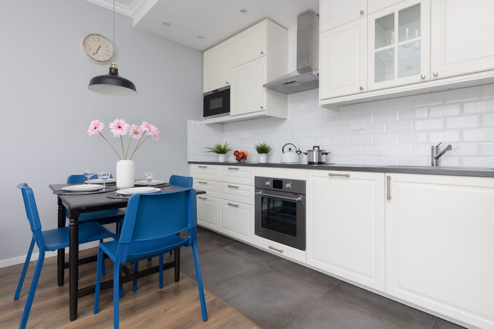 A modern kitchen with white cabinetry, a tiled backsplash, and a dining area with blue accents.
