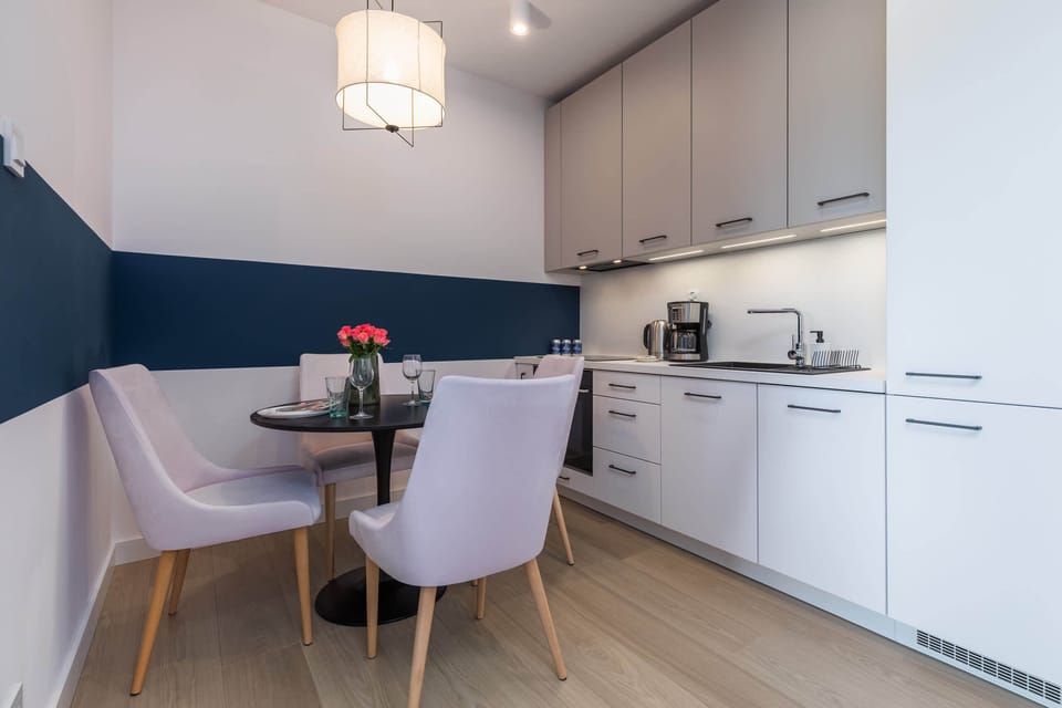 A modern dining area with a white table, elegant chairs, and a minimalist kitchen in the background.
