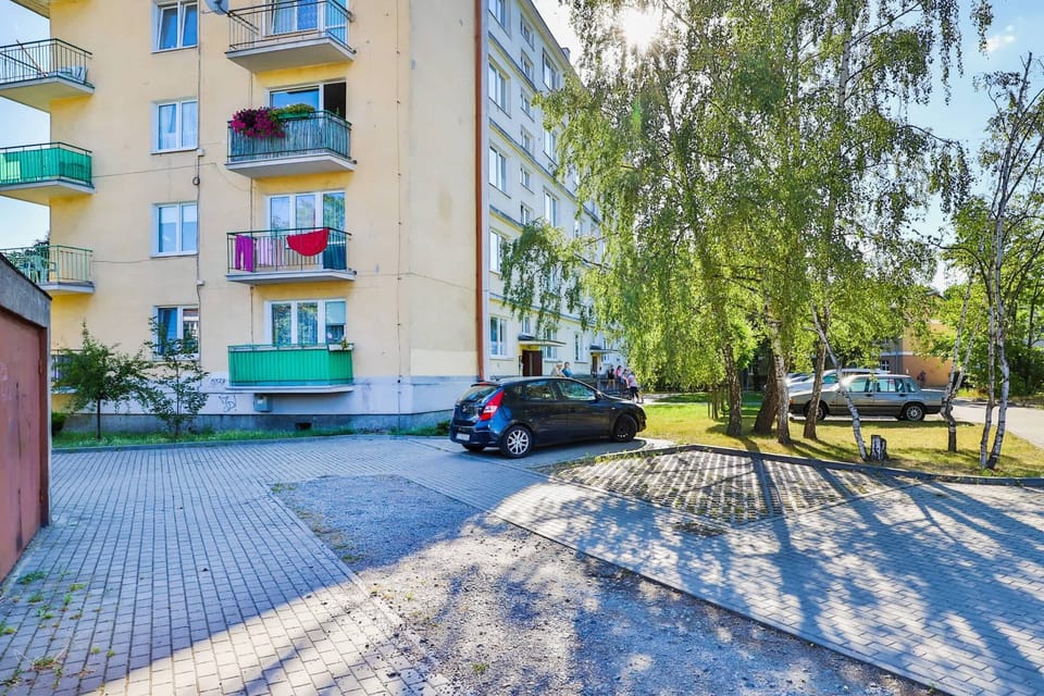 The exterior of the residential building, surrounded by a well-maintained parking area and greenery.
