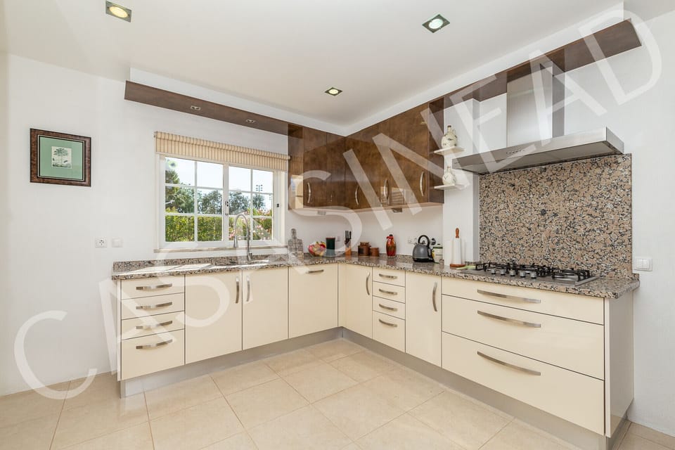 Spacious kitchen in Casa Sinead with cream cabinetry, granite worktops, stainless steel appliances, and extractor hood, offering ample storage and workspace for self-catering holidays in the Algarve