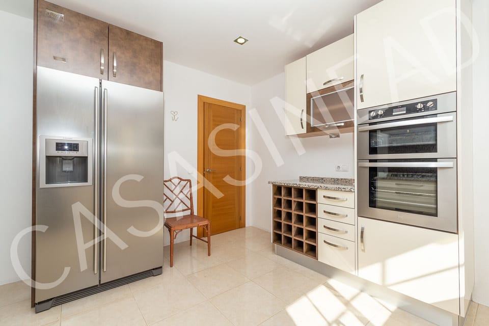Fully equipped kitchen in Casa Sinead featuring a stainless steel American-style fridge-freezer, built-in oven, wine rack, and sleek white gloss cabinetry, ideal for preparing meals during your Algarve holiday