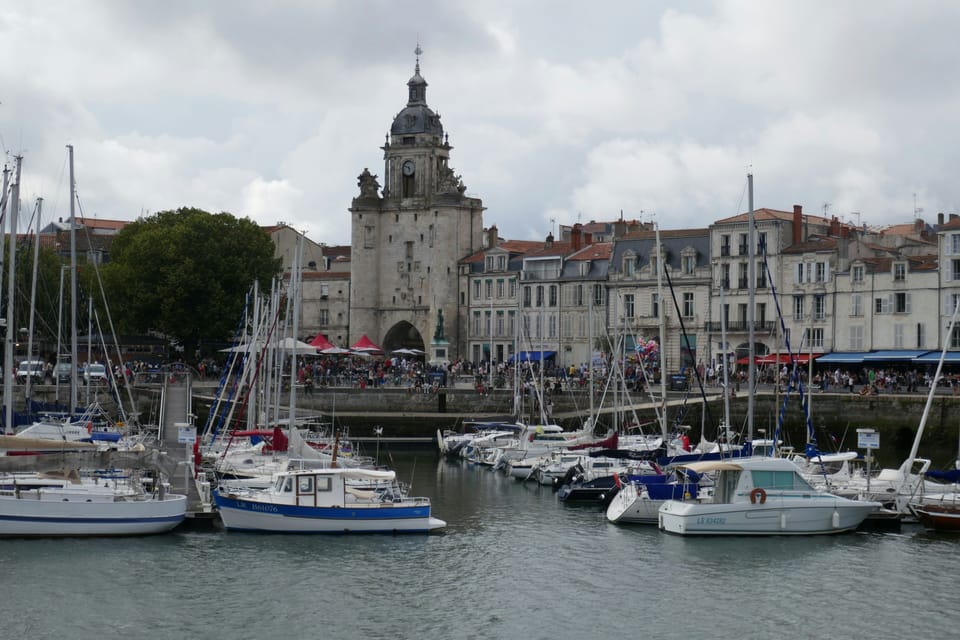 Sailboats moored at the old harbor with the Tour de la Lanterne and historic waterfront buildings in the background