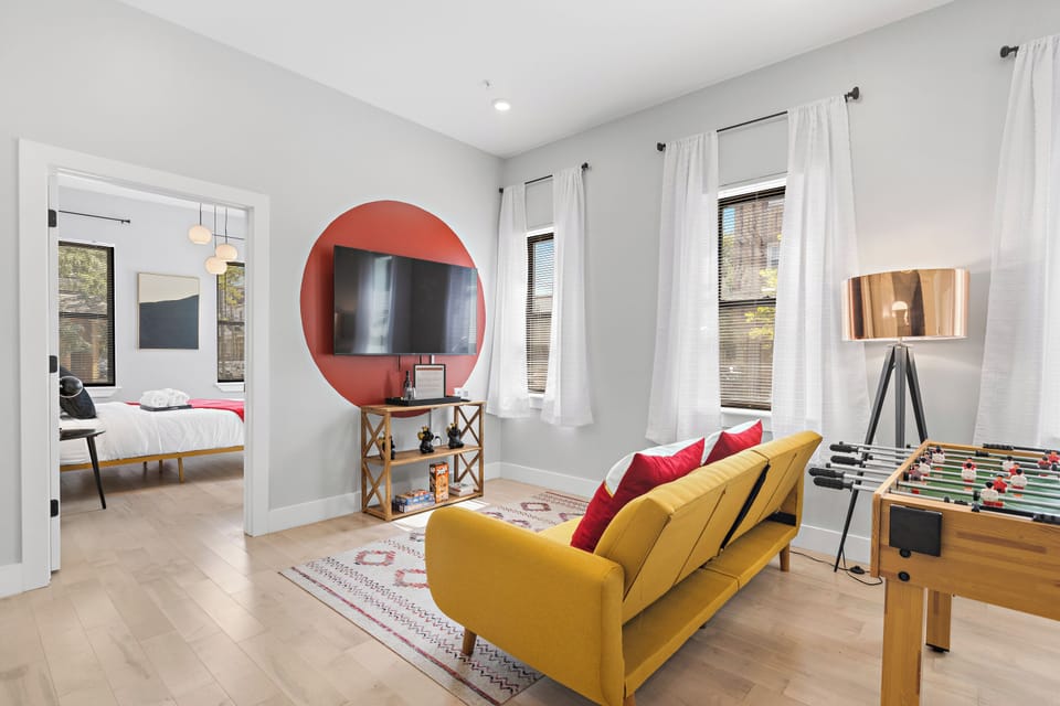 Welcoming living room flooded with natural light, featuring a state-of-the-art smart TV for entertainment, and a lively foosball table, creating a perfect space for relaxation and fun gatherings.




