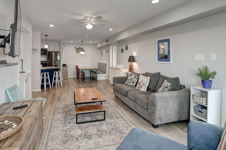 Unwind in your stylish open-plan living space, where modern comfort meets coastal charm with a cozy sofa and fully equipped kitchen.