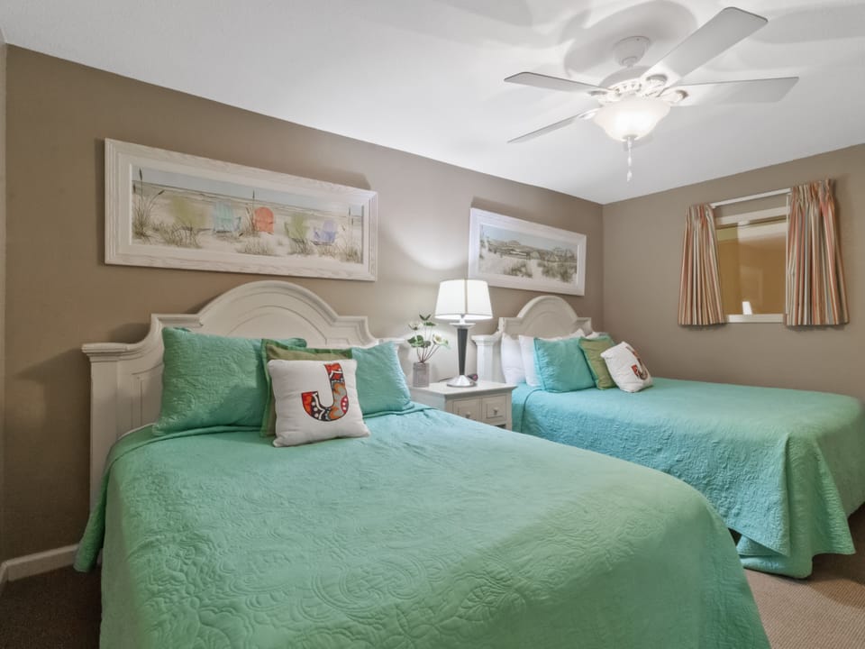 Relax in your coastal twin bedroom with cheerful turquoise bedding, beachy artwork, and gentle ceiling fan keeping you comfortable.