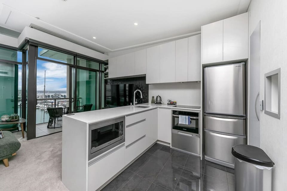 Cook with a view in this sleek penthouse kitchen -- stainless steel appliances gleam beside white stone countertops while the Viaduct Marina sparkles through the glass beyond.