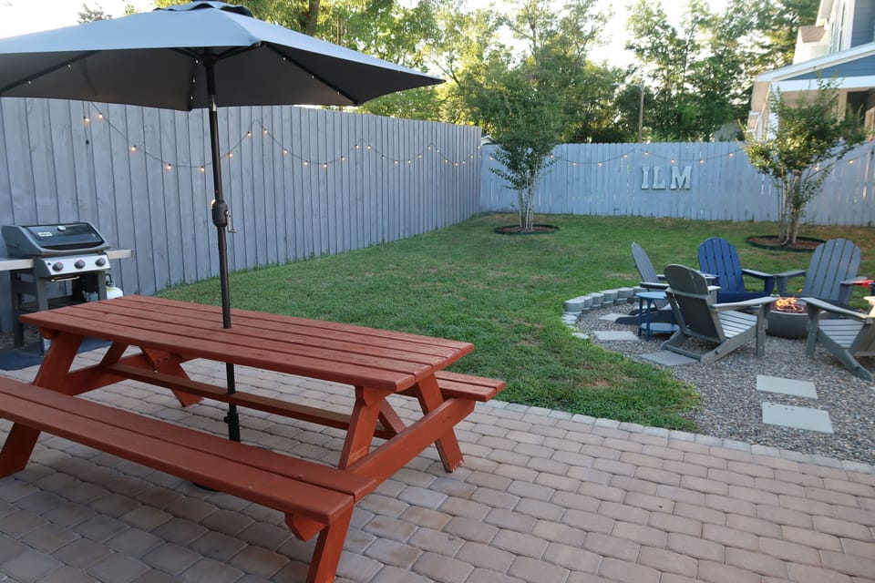 Large picnic table with umbrella. Six chairs in the river rock propane fire pit area