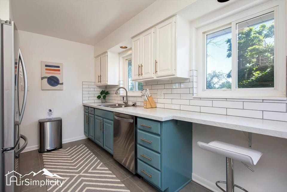 - Chic galley kitchen with two tone cabinetry, subway tile backsplash, and sleek counters
- Stainless appliances and bar seating make cooking and socializing easy
- Large windows bring in sunlight and frame views of the backyard greenery

