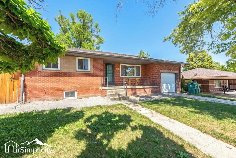 - Welcoming red brick exterior with covered porch and steps up to the front door
- Large picture window brings in natural light and neighborhood charm
- Driveway and attached garage provide easy parking and storage space