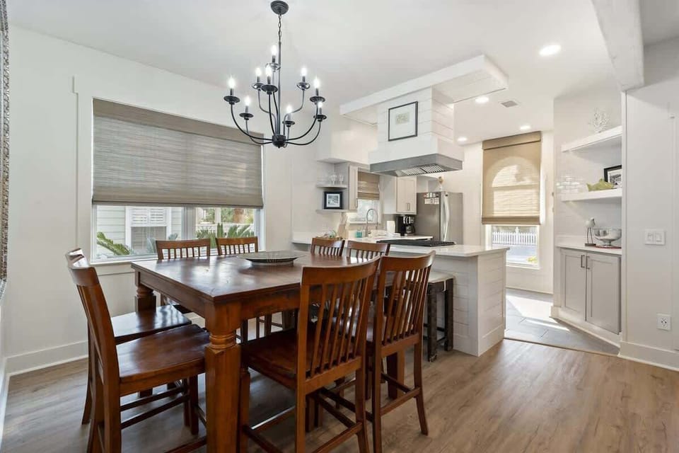 - Spacious wooden dining table comfortably seats eight for shared meals and family game nights - Dramatic black chandelier and soft window light create a warm, inviting setting - Open layout connects to kitchen and living areas for easy flow