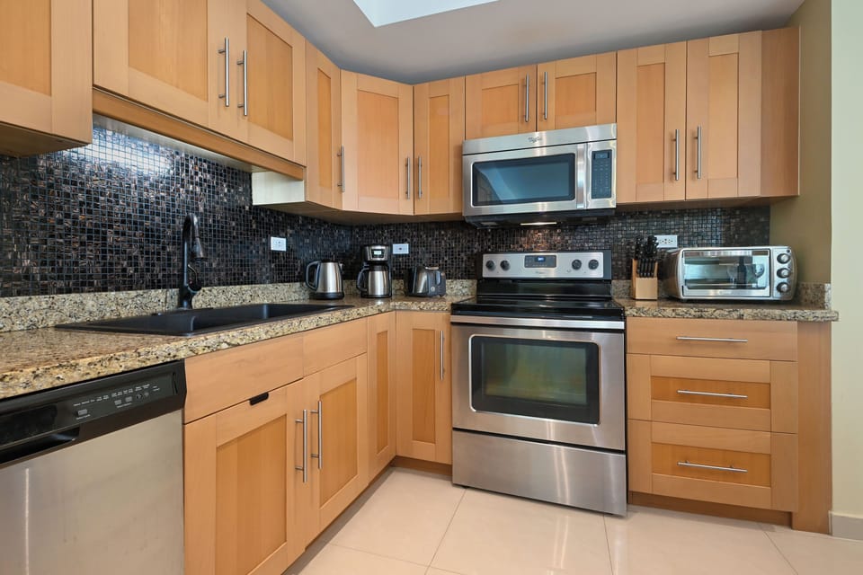 Your fully equipped kitchen features modern stainless appliances, gleaming granite countertops, and stylish mosaic backsplash—perfect for preparing meals during your stay.