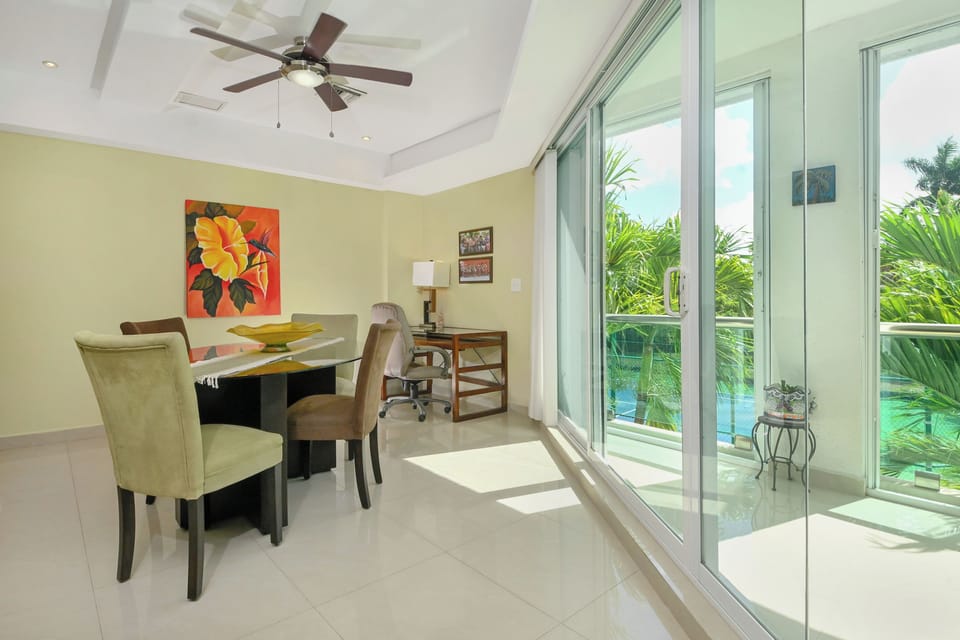 Step into your bright dining space where tropical breezes flow through floor-to-ceiling glass doors. Your private pool awaits just beyond the balcony, framed by lush palms.