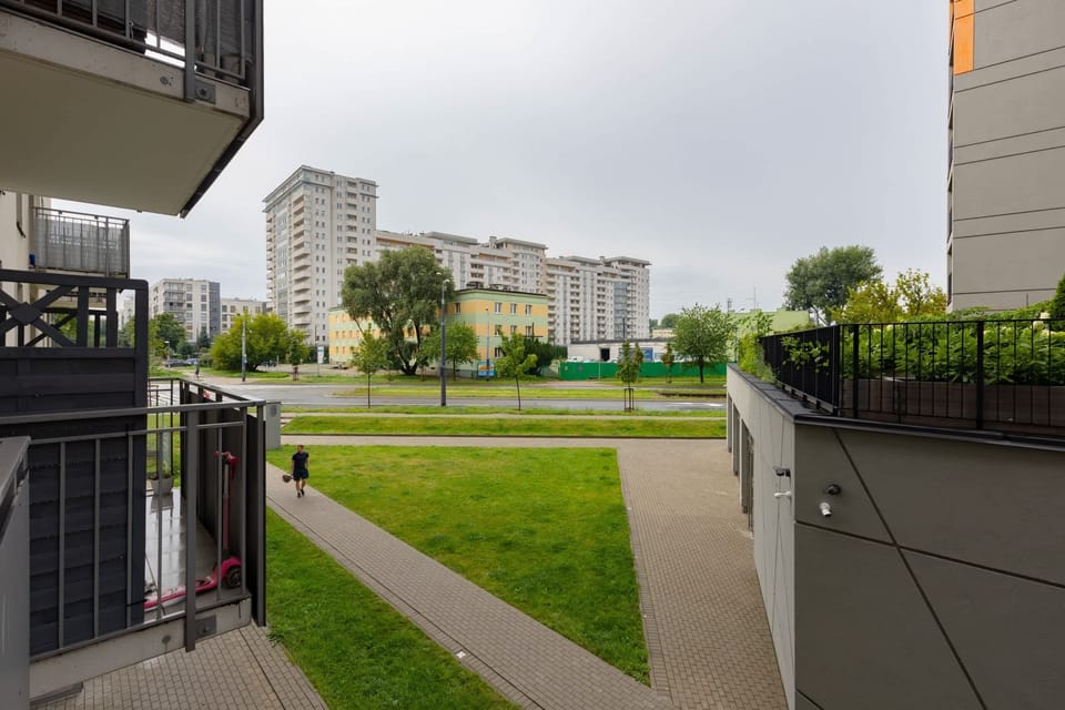A green outdoor space leading to the building's entrance, with a view of modern apartments.
