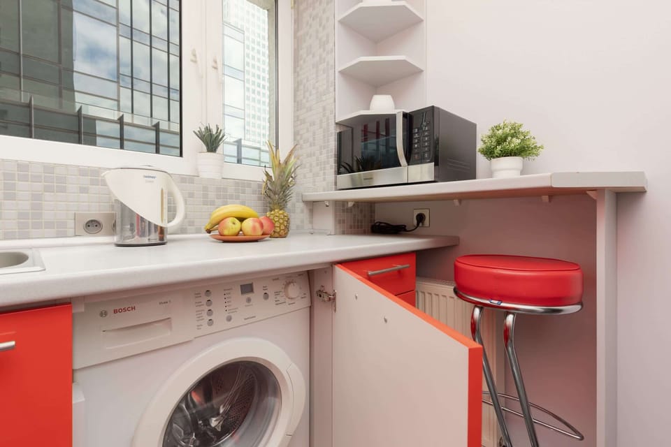 Another angle of the kitchen, featuring a breakfast bar with a red stool, a washing machine, and stylish decor.

