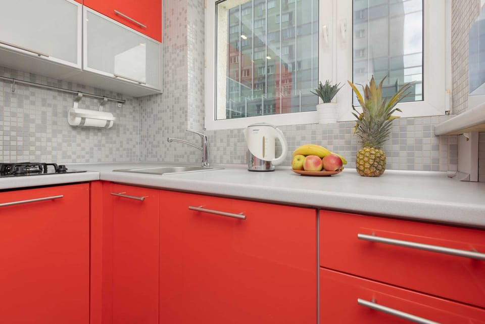A sleek kitchen with vibrant red cabinets, marble countertops, and a window providing ample natural light.
