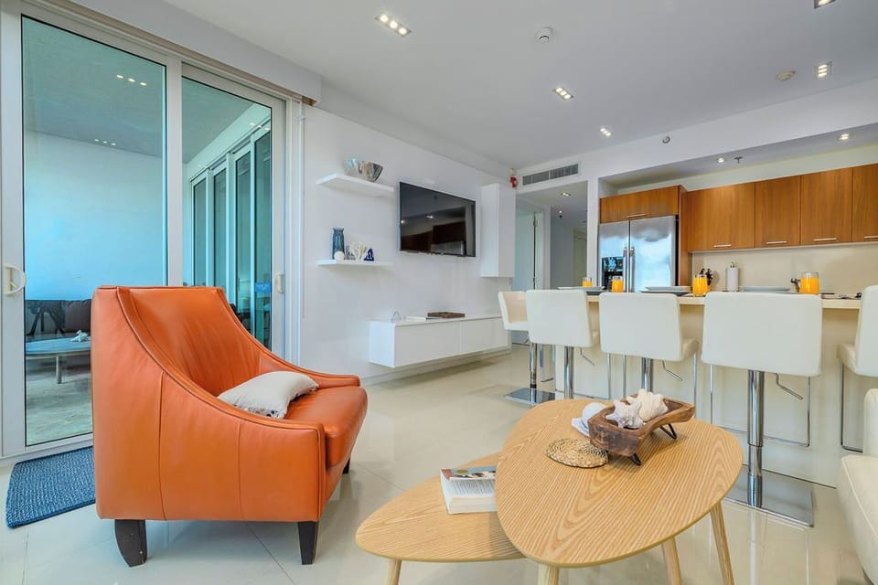 Sink into the vibrant orange chair and enjoy your morning coffee at the sleek breakfast bar in this modern, light-filled living space.