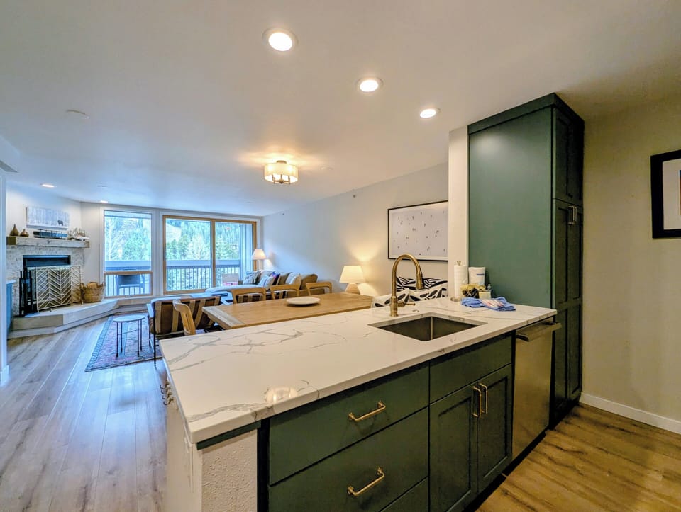 Your modern open-concept living space features stylish green cabinetry, gleaming marble countertops, and forest views—perfect for preparing meals while staying connected to your group.