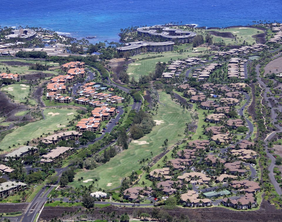 Oceanfront resort community nestled along championship golf fairways with tropical landscaping, beachside facilities, and panoramic coastal views defining the arrival area.