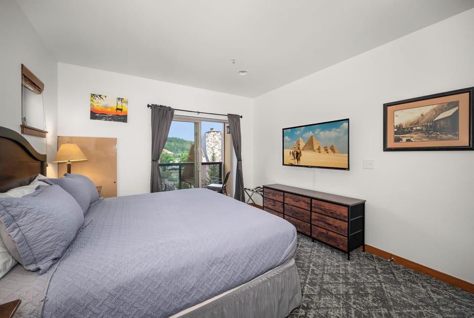 Bright king bedroom with TV, natural light, and scenic balcony views