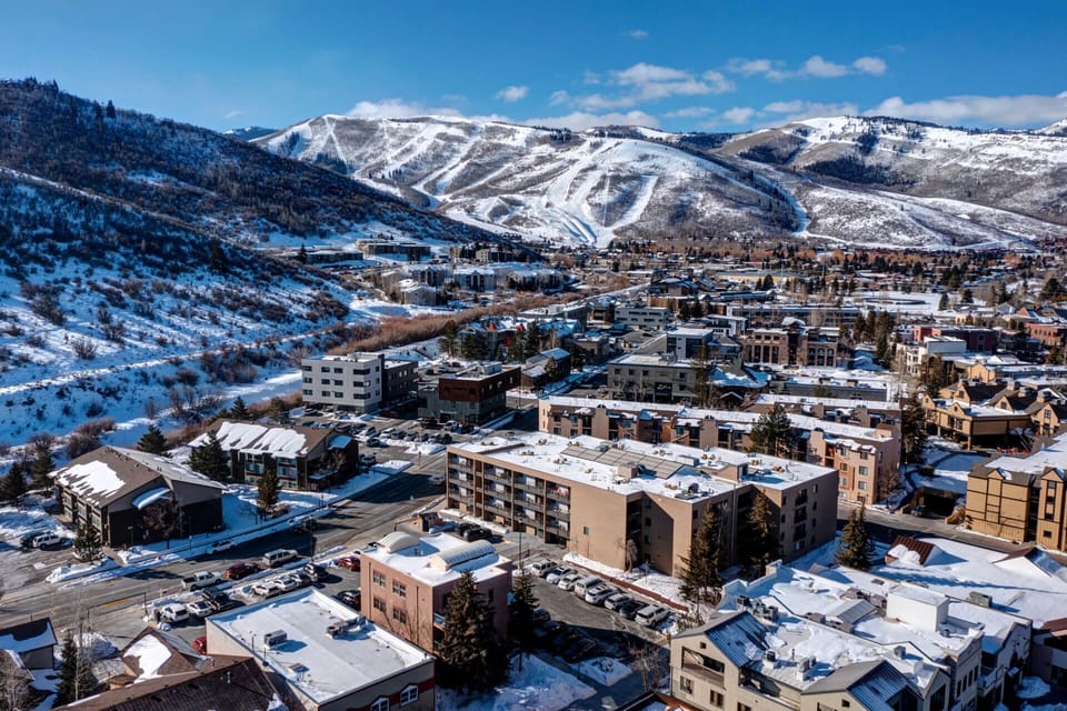 A charming mountain town nestled in a snowy valley, with ski slopes carving down distant peaks and cozy lodges dotting the landscape below.
