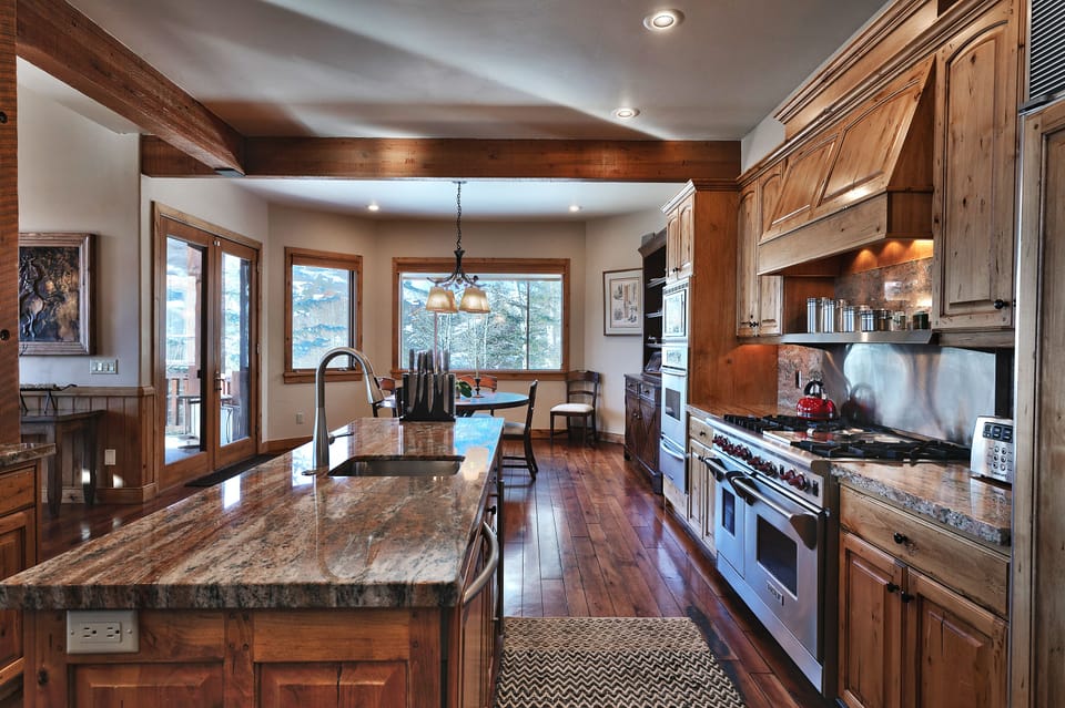 Middle kitchen island with granite countertops, sink, 6 burner Wolf range, medium wood cabinets and hard wood floors.