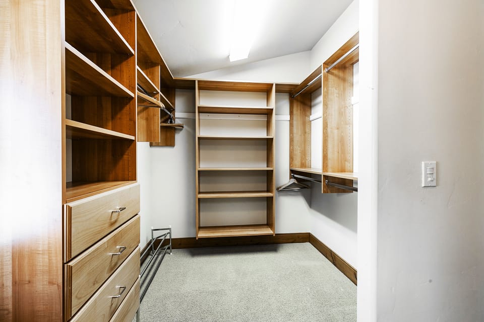 Walk in closet with built-in wooden storage cubbies, drawers, hanging rods, bright lighting and white walls.