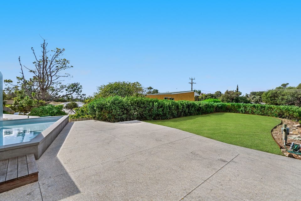 Front of home including infinity pool, large driveway and grass area