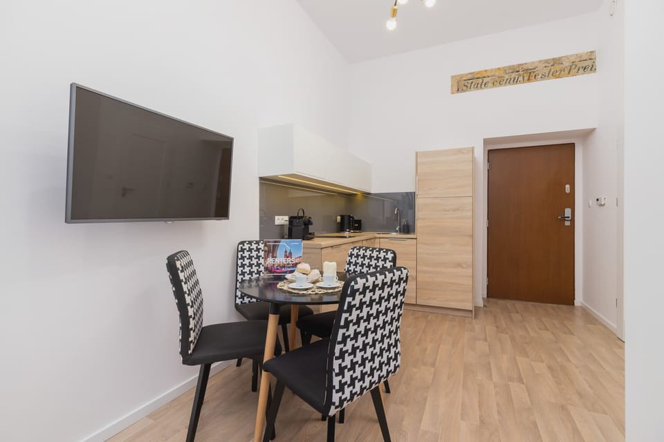 A bright open-plan area with a dining table, chairs, and TV, connected to the entrance. The wooden flooring brings warmth to the interior.